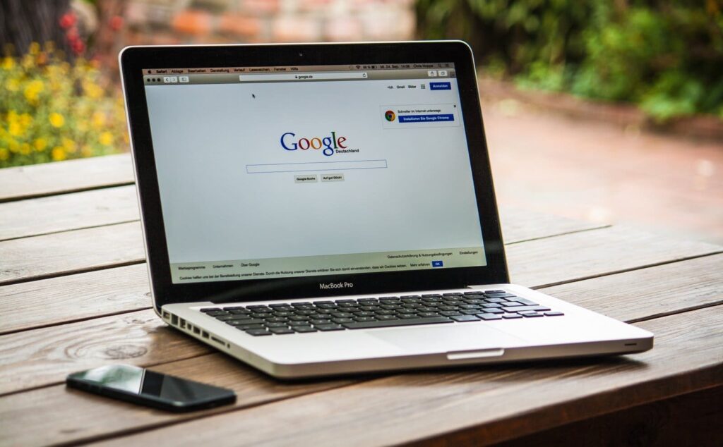 Ordenador portátil abierto sobre una mesa de madera con el buscador de Google en primer plano.